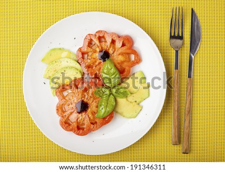 Salad mix with avocado and Beefsteak tomato , with balsamic dressing. on white plate &  yellow background. Light summer salad. olive oil. basil leaf. half avocado.