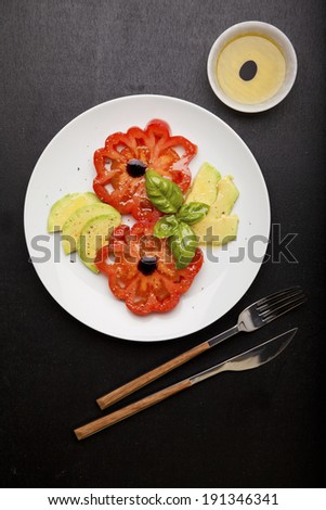 Salad mix with avocado and Beefsteak tomato , with balsamic dressing. on white plate & dark background. Light summer salad. olive oil. basil leaf. half avocado.