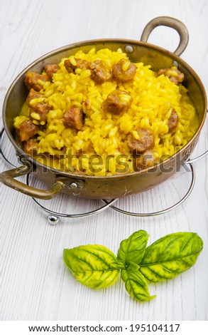 risotto with homemade sausage and saffron in little old pan. on a white wooden background. Italian cuisine. parmesan cheese. white wine. fresh basil leaves. dishware.zafferano. Italian yellow risotto