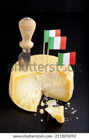 whole of parmesan with handle cheese knife & italian flag. on black. pecorino cheese.