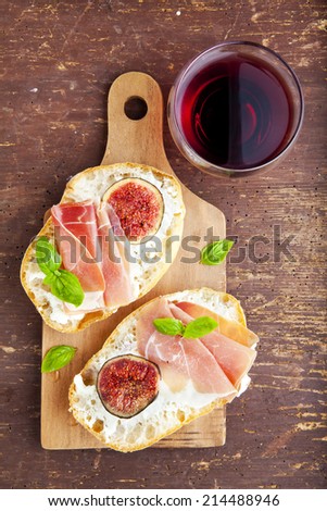 bruschetta with prosciutto ham & figs with white cheese. fresh basil.  red wine in the glass. italian appetizer.
