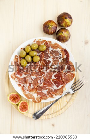 Italian snacks. Prosciutto, green olives, figs on wooden plate