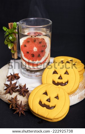 hot drink with red orange, star anis & Cloves and halloween pumpkin cookies, decorated cinnamon and mint on dark