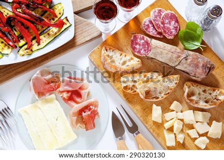 Italian healthy snacks. prosciutto, salami, vegetables grilled peppers and zucchini, parmesan cheese, fresh sliced bread ciabatta, ripe basil, and Marsala wine in glasses. Summer breakfast or lunch