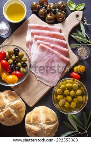 Wine appetizer set. Antipasti Platter of baked ham, red and yellow cherry tomatoes, Black Sicilian tomatoes, black and green olives, the leaves of the olive tree, salt and pepper, bread turtle.