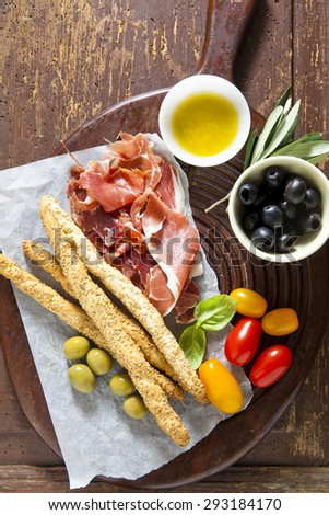 prosciutto crudo on a wooden board. Serving a snack. olives, tomatoes, olive oil. breadsticks. Natural Health Food Italy