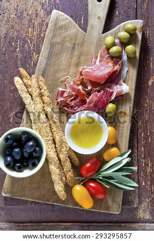 cured meat on a wooden cutting board with red tomatoes, olives and other ingredients for a lunch snack. on an old tree.