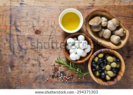 Food ingredients on the wooden background. small mozzarella, mushrooms, green and black olives. olive oil. small mozzarella, mushrooms, green and black olives. space for writing or placing text menu.