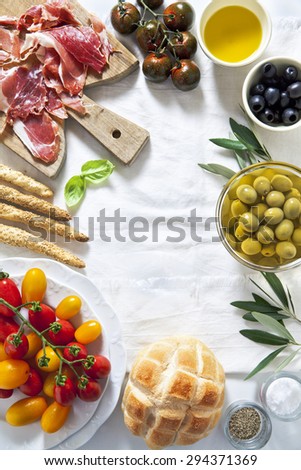 prosciutto crudo with bread, olives, tomatoes, bread sticks, olive oil and basil on a white tablecloth. space for writing text.