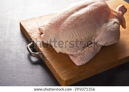 raw whole chicken ready for roasting on a wooden board on a black background