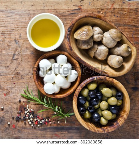 Food ingredients on the wooden background. small mozzarella, mushrooms, green and black olives. olive oil. small mozzarella, mushrooms, green and black olives. space for writing or placing text menu
