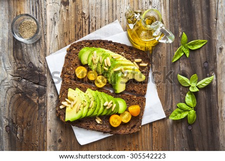 sandwich with rye bread on old wooden table: avocado, yellow tomatoes, pine nuts and honey. healthy vegetarian food. space for writing the text, placing the menu.