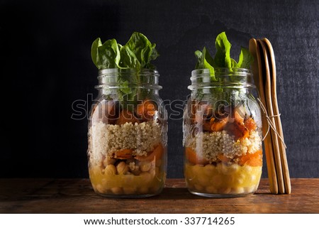 Mason jars with hot Salad: Chickpeas, carrots, quinoa, roasted Pumpkin and spinach. Ripe red currants . Healthy Lunch. falling leaves of basil