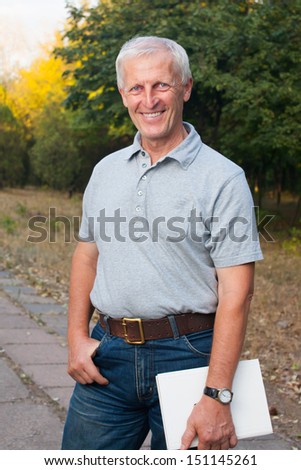 Happy emotional old man smiling. Posing in the park. Outdoor. Blue jeans. Grey t-shirt. Watch
