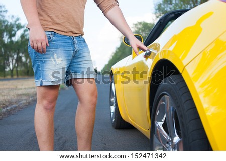 Closeup of Young Man open convertible cars door. Yellow car. Brown t-shirt, jeans shorts