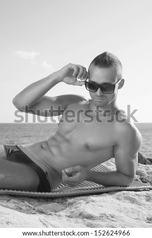 Perfect body guy lying on beach. Black and white