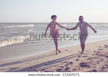Happy couple in sunglasses. Run on the beach holding hands. Dynamic shot outdoors