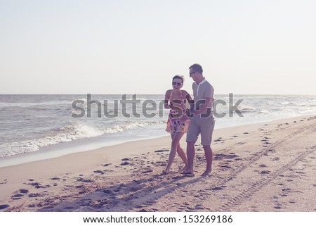 Dynamic shot of happy smiling couple. Focus on guy. Walking on the beach. Holding each other and laughing