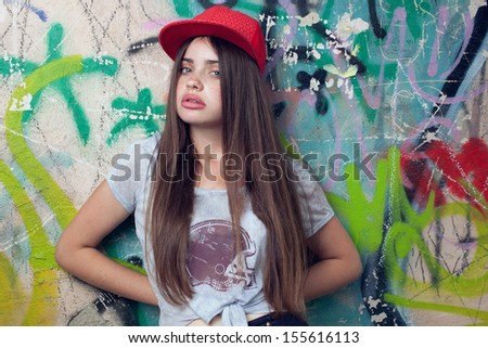 trendy beautiful long haired model posing near painted  wall. red cap. grey t-shirt.