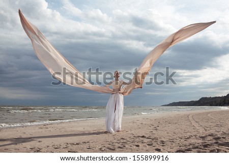 female model in extreme long beige dress posing dynamic in the beach. waving fabric. fluttering long skirt like a wings