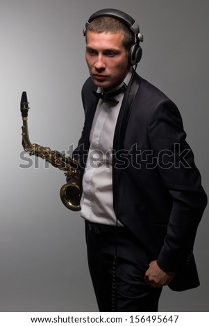 Portrait of young saxophone player with headphone in tuxedo. DJ with sax
