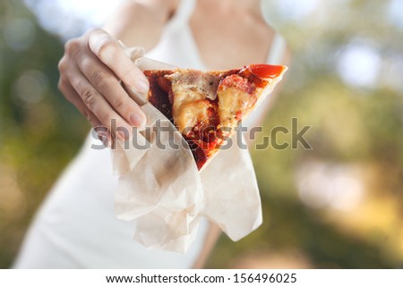 Woman\'s hands holds piece of homemade pizza with tomato, bacon, salami and cheese. Outdoors