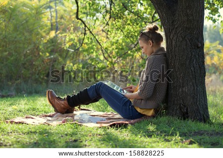 Hipster girl leaning on a tree and using tablet computer Hipster girl leaning on a tree and using tablet computer