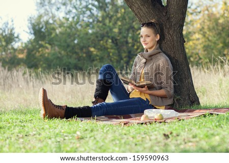 Young woman have rest with book under the tree during picnic