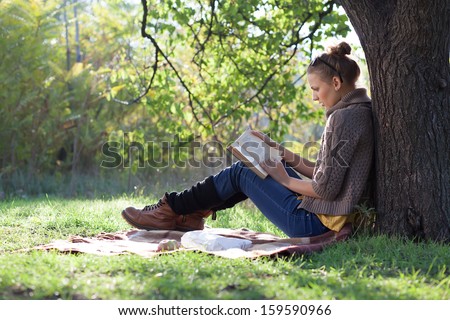 Young woman reading book under the tree during picnic in evening sunlight