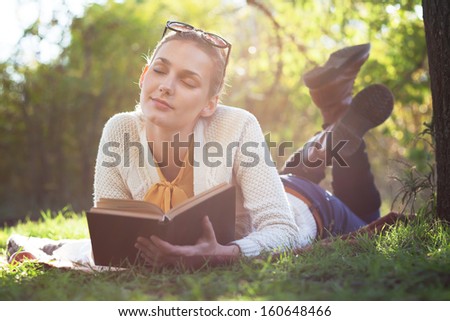 lying girl dreaming with book under the tree in evening sunlight outdoors