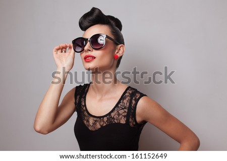 Young fashionable woman in round sunglasses posing in guipure dress. Red lips. Updo, twisted high bun. top knot