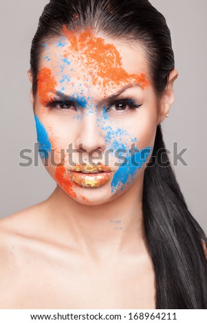 Beauty shot of emotional female face with orange and blue dry powders. gold glitters on lips. FaceArt