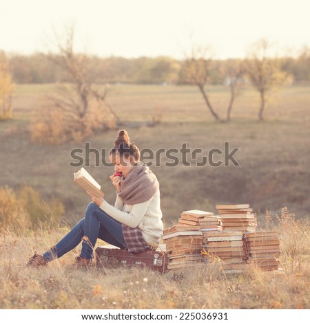 Young woman reading a books and eating apple outdoors