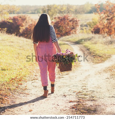 Hipster girl steps by road with basket of flowers