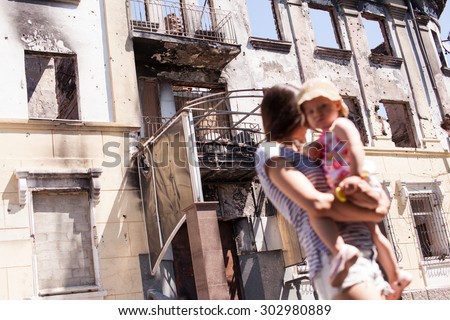 MARIUPOL, UKRAINE - JULY 19, 2015: Mother with baby walking near of destroyed building of Mariupol Police City Department