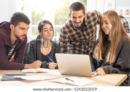 Happy young university students studying with laptop in library. Group of multiracial people in college library sitting together at table with books and laptop. Happy young people.
