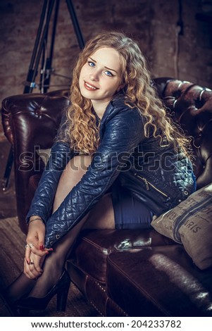 Girl with long blond hair in a leather jacket sitting on the couch leaning on the arm