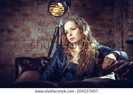 Girl with long blond hair in a leather jacket sitting on the couch leaning on the arm