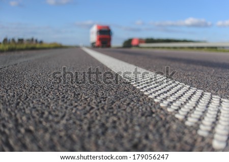 close-up asphalt with dotted white stripe. Red truck on the horizon