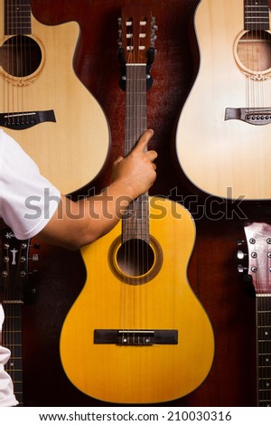 Man hand holding acoustic guitars hanging on a wall.