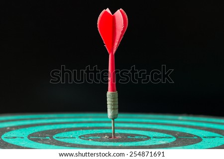 Red dart arrow hitting in the center of green dartboard.
