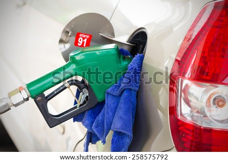 Fueling nozzle inserted into petrol tank at gas station for gasoline filling with cleaning cloth.