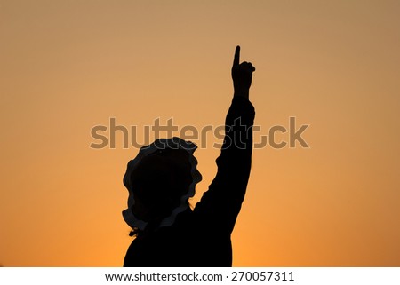 Silhouette woman pointing her finger up to sunset sky background.