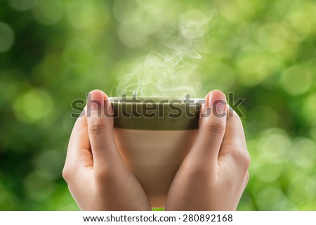 Hands holding tea cup on green bokeh background.