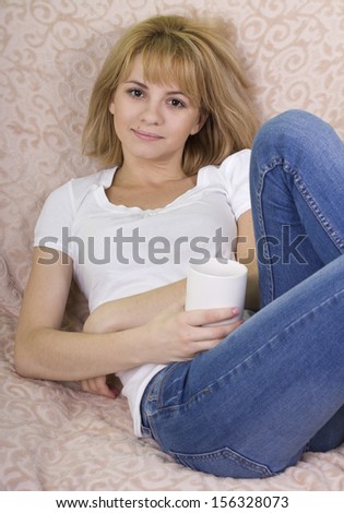 beautiful blonde with a white cup in hand resting on the couch at home