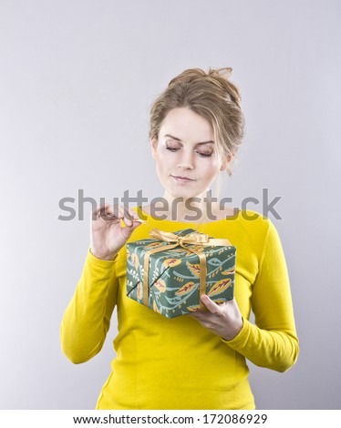 beautiful young blond woman in a bright yellow blouse with colorful gift in hand on gray background