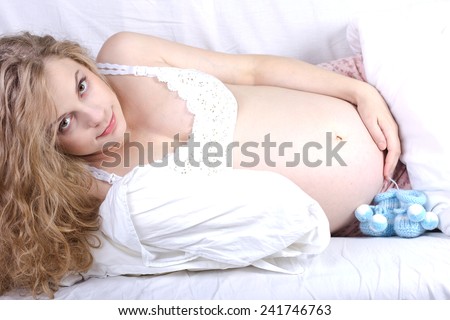 young pregnant woman luxuriates in a white bed.Woman Bed Portrait.Beautiful pregnant curly blonde