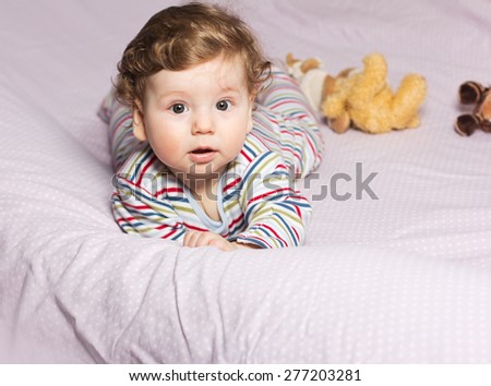 Beautiful child in crib with toys. Cute boy. Curly blonde. Portrait of a baby