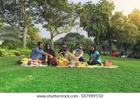 Young family with baby having picnic on green grass meadow in nature, cheerful concept, Arabic family