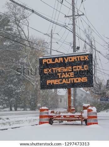 Electric road traffic mobile sign by the side of a snow covered road with snow falling warning of polar vortex, extreme cold take precautions